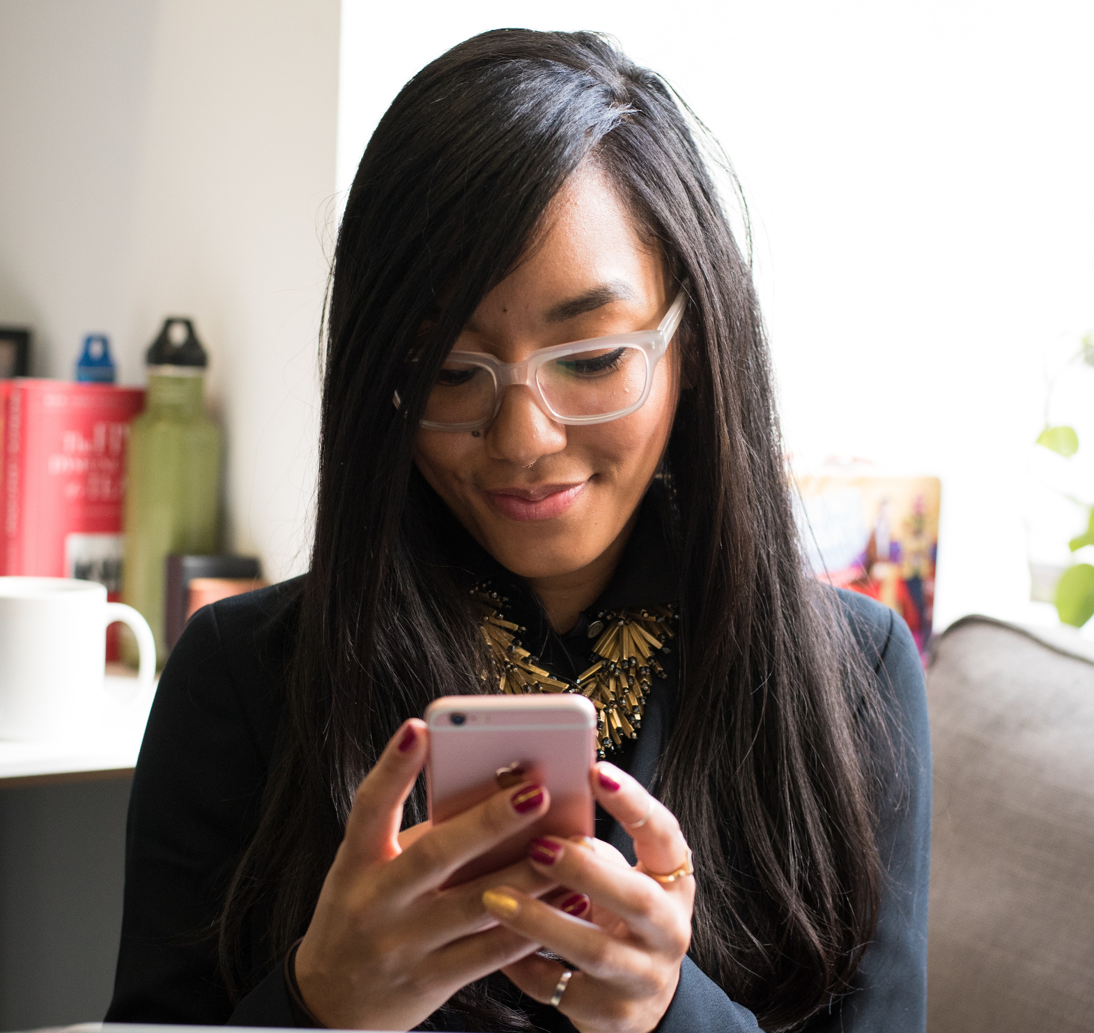 Woman with dark hair sitting on a sofa texting on her phone